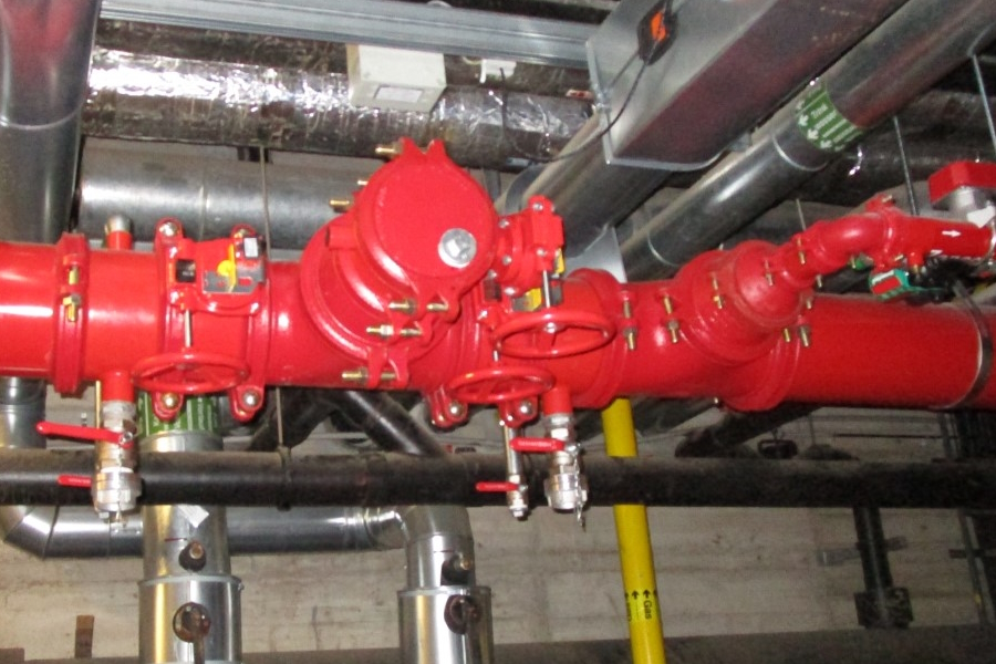 Zu sehen ist ein Teil einer Sprinklerleitung, ein Rohr in der Farbe Rot mit mehreren Ventilen.