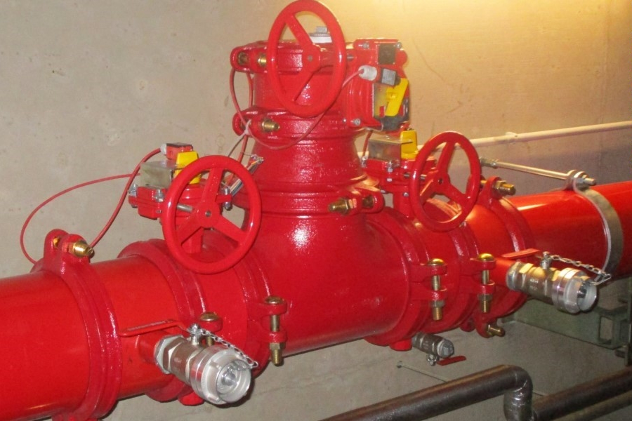 Zu sehen ist ein Teil einer Sprinklerleitung, ein Rohr in der Farbe Rot mit mehreren Ventilen auf der Höhe des Torsos.